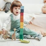 Child in White Long-sleeve Top and Green Dungaree Trousers Playing With Lego Blocks and Toys